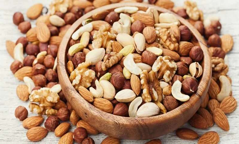 Photo of a bowl full of mixed nuts, some overflowing to the table