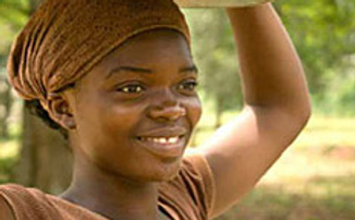 Photo of smiling Afro-Caribbean woman, possibly carrying something on her head, but that is cropped out.